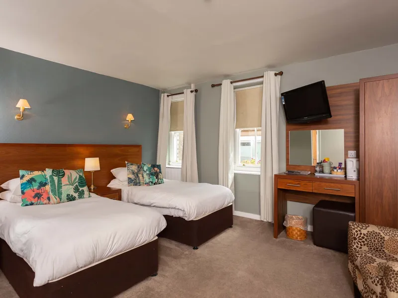 A twin room at the Queens Head with teal walls, tropical-print cushions, desk and TV