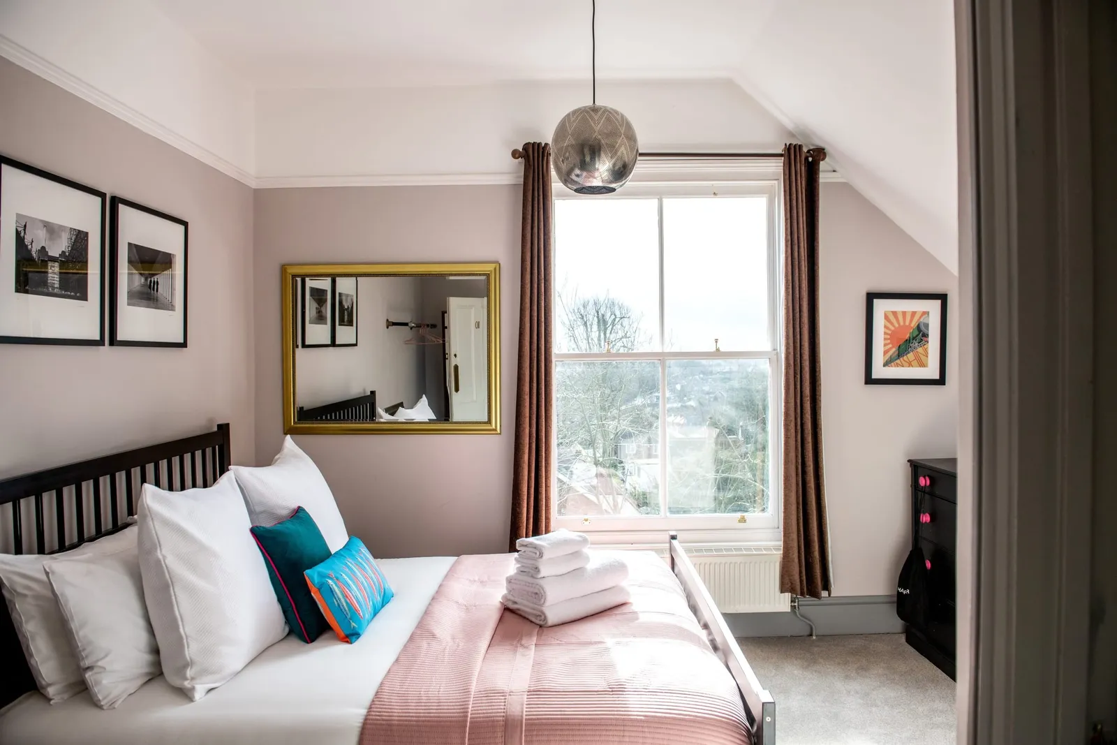 A bedroom at the Royal Oak with a black iron bed, pink throw and a window over the village