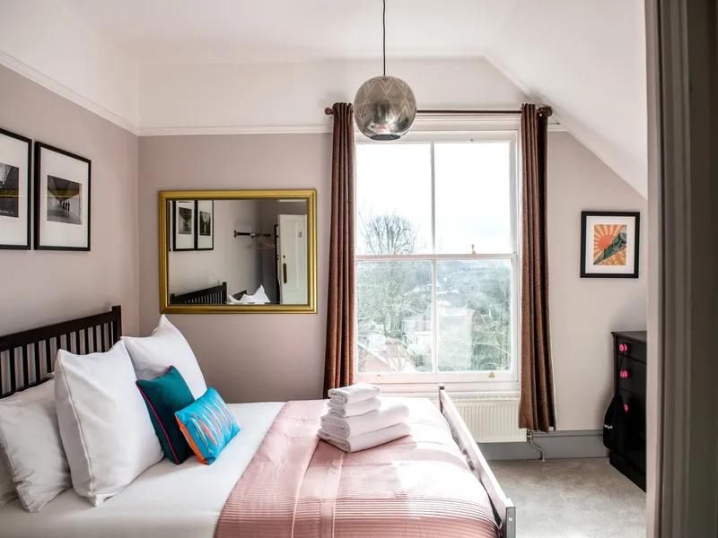 A bedroom at the Royal Oak with a black iron bed, pink throw and a window over the village