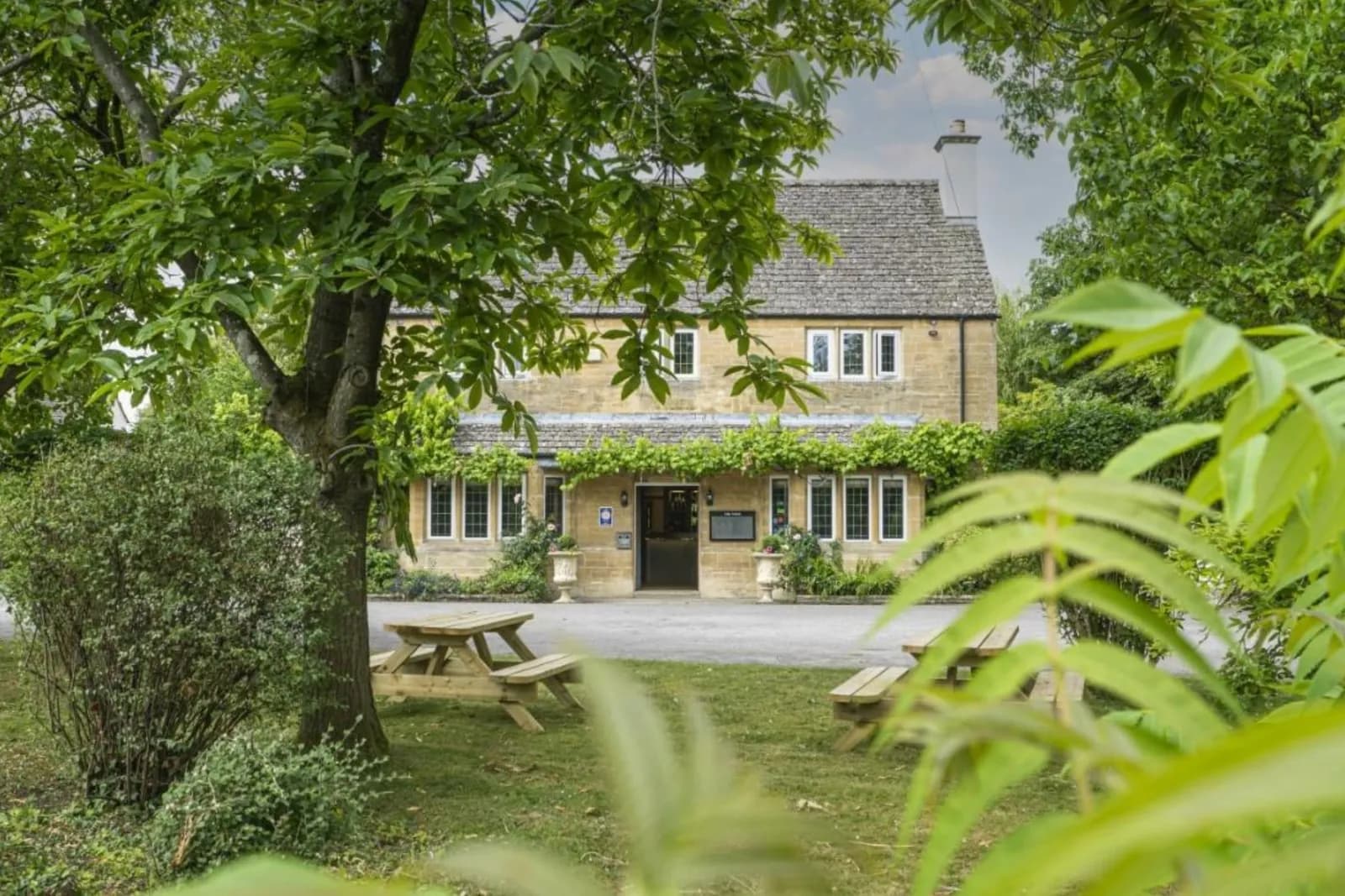 The Vines at Black Bourton, a stone Cotswold house seen through the trees